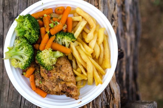 A delicious plate of chicken, fries, and fresh vegetables served on a rustic wooden table, ideal for a healthy meal.